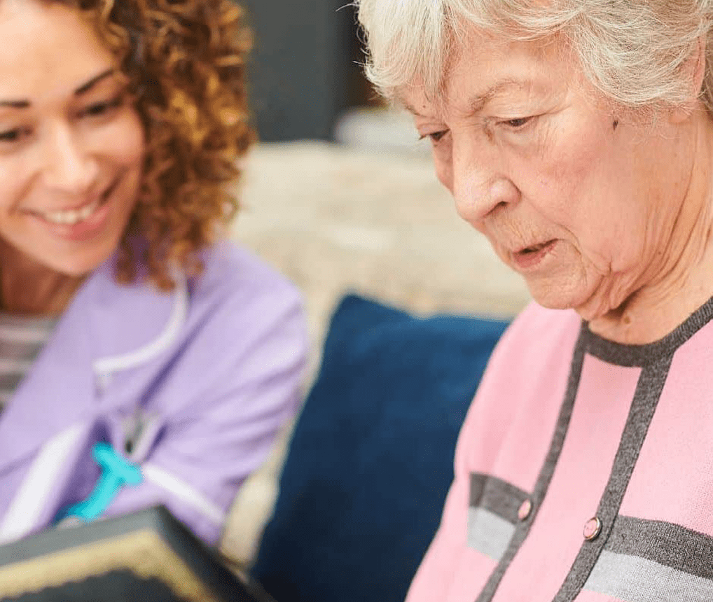 Elderly woman and caregiver reading together.